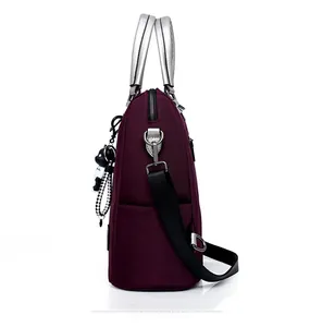 Vue latérale du sac bandoulière en nylon bordeaux avec poignées argentées et breloque ours