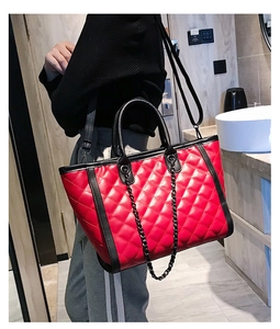 Détail macro du sac cabas rouge en cuir matelassé avec chaîne en métal noir et coutures