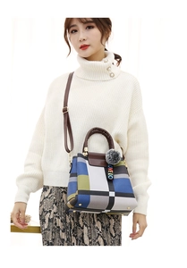 Detail of geometric plaid handbag with brown handles and a grey pompom charm