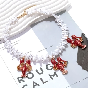 Detailed macro view of baroque pearl necklace featuring three red enamel lobster pendants