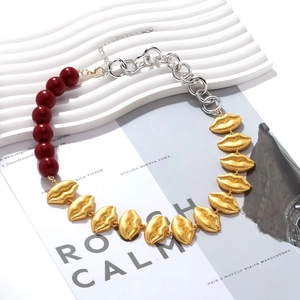 Exaggerated necklace with red beads, silver chain, and golden lip pendants on a card