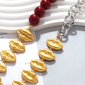 Detail of red bead and silver chain necklaces with gold matte lip charms on white board