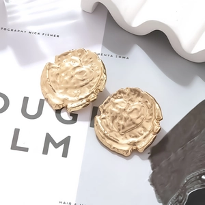 Golden irregular coin earrings with hammered texture and heart detail on white prop