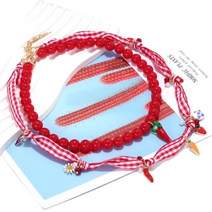 Double-layered beaded necklace featuring red beads, fabric ribbon, and enamel fruit charms