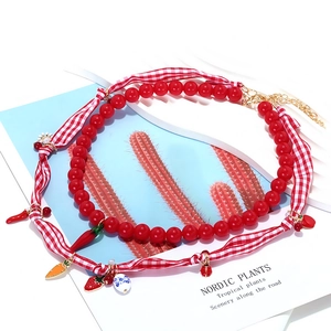 Detail of beaded necklace with strawberry and ladybug charms on red gingham ribbon