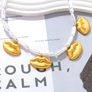 Collier perles baroques et pendentifs lèvres dorées sur fond de magazine