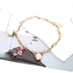 Vue détaillée du collier à maillons dorés avec pendentifs pêches en émail rose