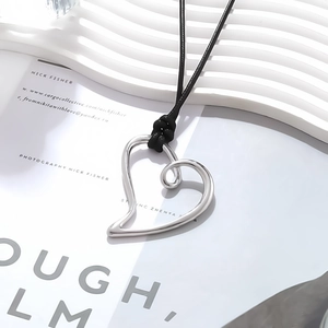 Close-up of a silver-tone hollow heart pendant on a black cord with elegant magazine background