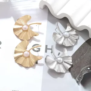 Detailed view of gold and silver ginkgo leaf earrings with pearl accents on art magazine