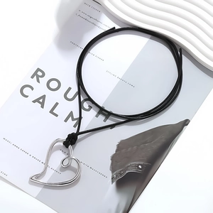 Minimalist silver heart pendant necklace with black cord shown on an aesthetic magazine background