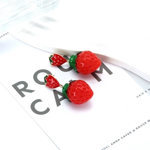 Vue détaillée des boucles d'oreilles fraise émaillée rouge sur un fond de magazine chic