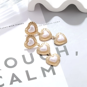 Macro detail of triple heart layered drop earrings with gold finish and baroque pearls