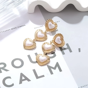Detailed close-up of triple heart-shaped pearl drop earrings with textured gold edges