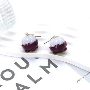 Minimalist purple mangosteen fruit drop earrings with gold hooks on a white wavy stand
