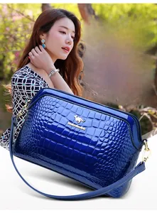 Close-up of blue patent faux crocodile leather handbag with gold metal logo and long strap