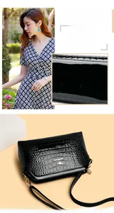 Detail of black faux crocodile leather crossbody bag with gold chain and metal logo