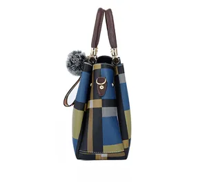 Detail of plaid tote bag with brown leather handles and grey faux fur pompom charm