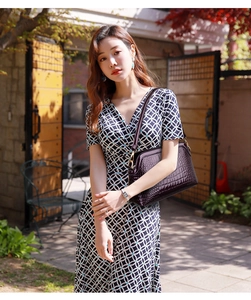 Detail of dark purple crocodile texture handbag held by model in stylish dress