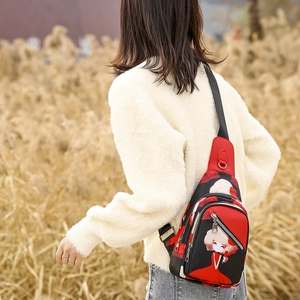Detail of red cartoon oxford chest bag with adjustable strap worn in outdoor setting