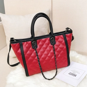 Grand sac cabas matelassé rouge avec chaîne noire sur une surface en peluche blanche