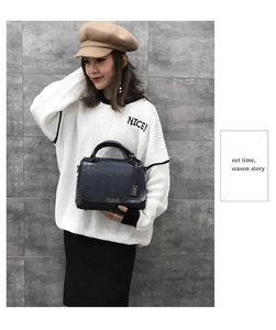 Détail d'un sac à main bleu foncé en cuir texturé avec fermoir en métal porté par un mannequin
