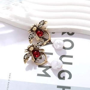 Boucles d'oreilles abeille vintage avec strass rouge et perle baroque sur un magazine