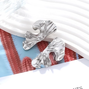 Macro shot of silver textured irregular geometric earrings with liquid metal abstract design