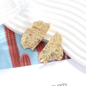 Exaggerated asymmetric gold alloy earrings with hammered texture on a white tray