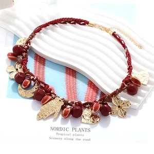 Detail of red braided bohemian necklace with gold charms like hand and heart on white decor