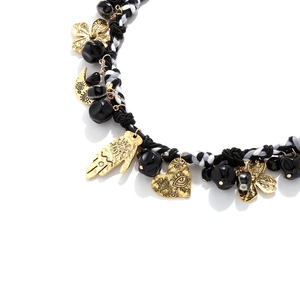 Macro shot of gold hand, moon and heart charms on a black and white braided rope necklace