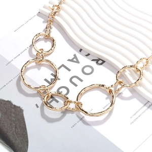 Golden geometric link body chain with textured lava circles on white artistic stand