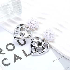 Detail of silver hollow heart earrings featuring handmade woven white bead spheres