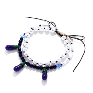 Double-layered pearl and blue bead necklace with purple eggplant charms on white background