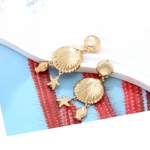 Boucles d'oreilles dorées coquillage et étoile de mer sur un présentoir blanc chic