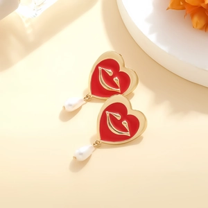 Detailed view of heart-shaped red enamel earrings with gold lips and teardrop pearls