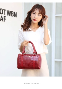Detail of red crocodile pattern patent leather Boston bag with gold brand plate on a model