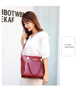 Detail of burgundy crocodile-pattern handbag with golden hardware worn by a model