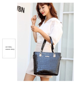 Detail of a black patent leather handbag with crocodile pattern held by a model