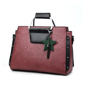 Détail du sac en cuir bordeaux avec anses noires contrastées et breloque étoile verte