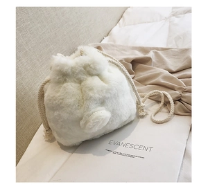 Detail of white faux fur bucket bag with drawstring closure and soft pom-pom charms