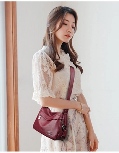 Detail of burgundy textured leather crossbody bag with golden kangaroo logo on soft fabric