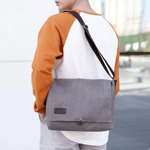 Men's grey canvas messenger bag worn by a model in an urban outdoor street setting