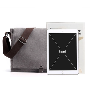 Gray canvas messenger bag for men with adjustable strap beside a tablet and magazine
