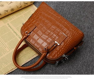 Close-up of brown crocodile embossed leather texture and silver zipper detail on handbag
