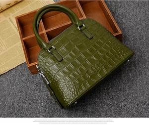Detailed close-up of dark green crocodile embossed handbag with metal zipper and sturdy handles