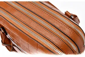Detail of brown leather handbag featuring silver zippers and embossed crocodile texture