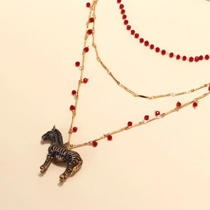 Détail macro d'un collier multicouche doré avec perles rouges et pendentif zèbre