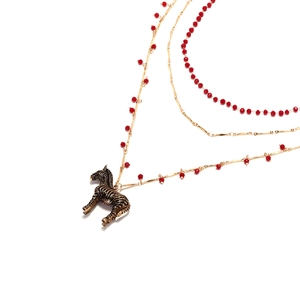 Collier multicouche doré avec perles rouges et pendentif zèbre sur fond blanc épuré