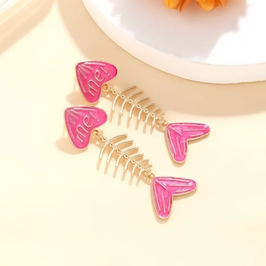 Macro view of pink enamel heart and golden fishbone earring details on a white stand