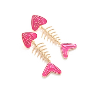 Macro view of pink enamel fishbone earrings with heart-shaped detail and me! engraving